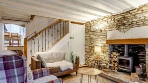 Ein gemütliches Wohnzimmer mit Steinwand, Kamin, einer Couch und einer Holztreppe.