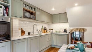 Eine Küche mit hellgrauen Schränken, einer weißen Fliesenrückwand, einem Edelstahlbackofen und einem Holzboden.