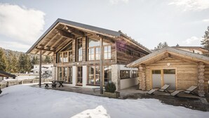 Une cabane en rondins dotée d’un grand porche, d’un espace extérieur couvert aménagé en salon, et dont le sol est recouvert de neige.