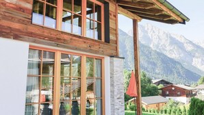 Une cabane en bois dotée de grandes fenêtres, d’un mur en pierre et offrant une vue sur la montagne.