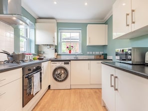 A compact kitchen with a washing machine, a stove, and a window with a view. - 3 Bed in Christchurch (oc-73946) (Christchurch)