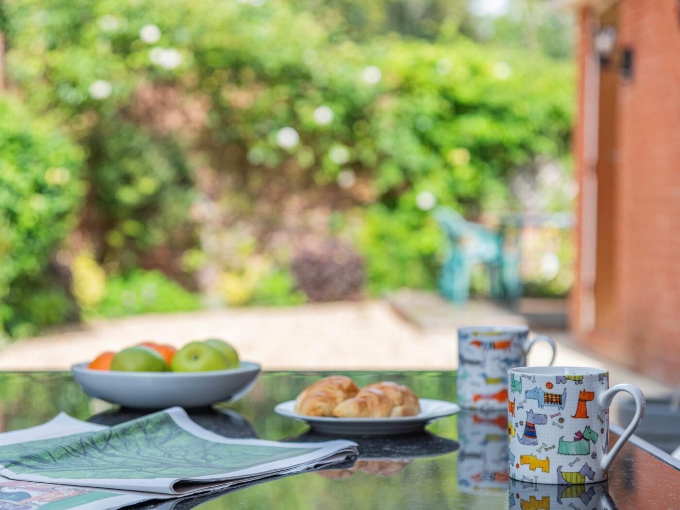 Ein Tisch mit einer Obstschale, einem Teller Croissants, einer Tasse und einer Zeitung.