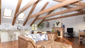 Um amplo loft com vigas de madeira aparentes, um sofá de couro, uma lareira e um espaço de jantar.