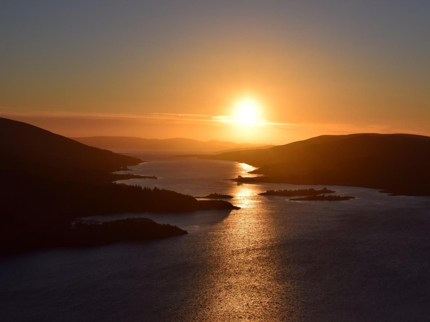 Un tramonto su acque calme, con colline che si estendono su entrambi i lati.