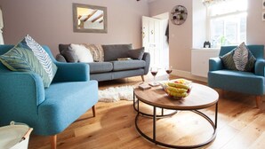 A living room with a grey sofa, two blue armchairs, a round coffee table with fruit, wooden flooring, and exposed wooden beams on the ceiling. - 2 Bed in Richmond (oc-74284) (Reeth)
