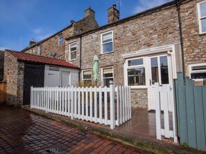 A stone-built residential building with a white picket fence, a red-tiled roof, and a green umbrella. - 2 Bed in Richmond (oc-74284) (Reeth)