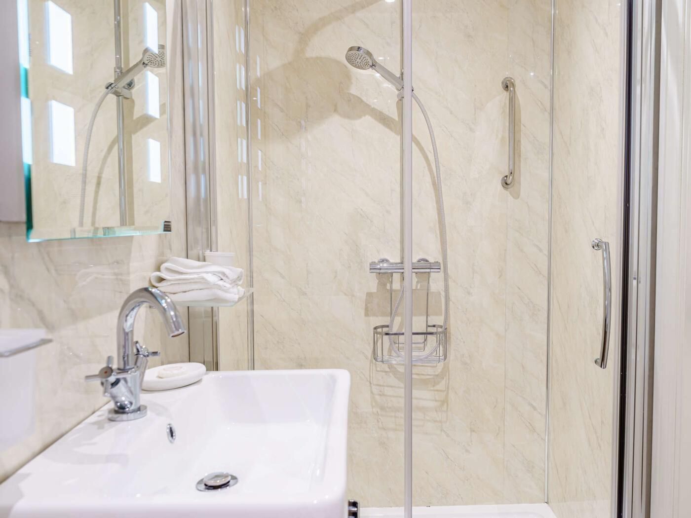 A bathroom with a glass-enclosed shower, a sink with a soap dish, and a towel rack.