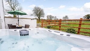 Een hottub met een houten omheining, een tafel met stoelen en een groene parasol.