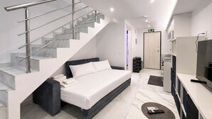 Una habitación de hotel moderna con una cama, un escritorio, un televisor y una escalera con barandas de vidrio.