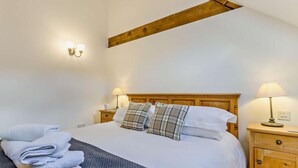 Ein Schlafzimmer mit einem Bett, zwei Nachttischlampen, einem Holz-Kopfteil, einem Nachttisch und einem zusammengelegten Handtuch auf dem Boden.