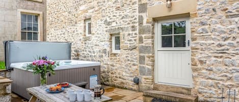 Un edificio de piedra con mesa de madera, jacuzzi y zona de estar al aire libre.