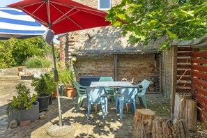 A patio area with a table and chairs, a red umbrella, and potted plants.