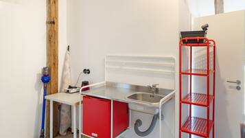 A compact kitchenette with a sink, a small storage unit, and a red metal shelf.