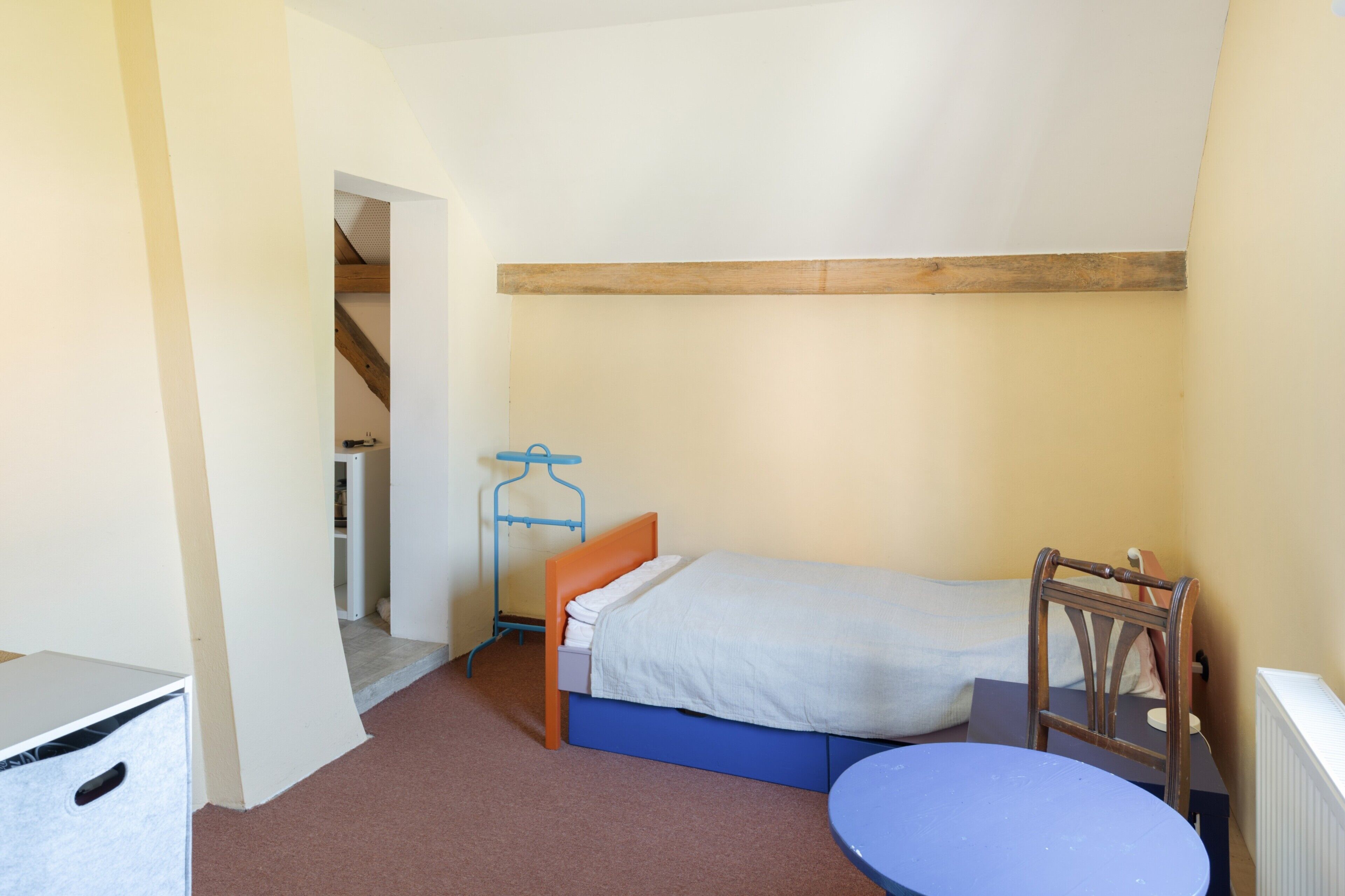 A small, compact room with a single bed, a small table, and a wardrobe.