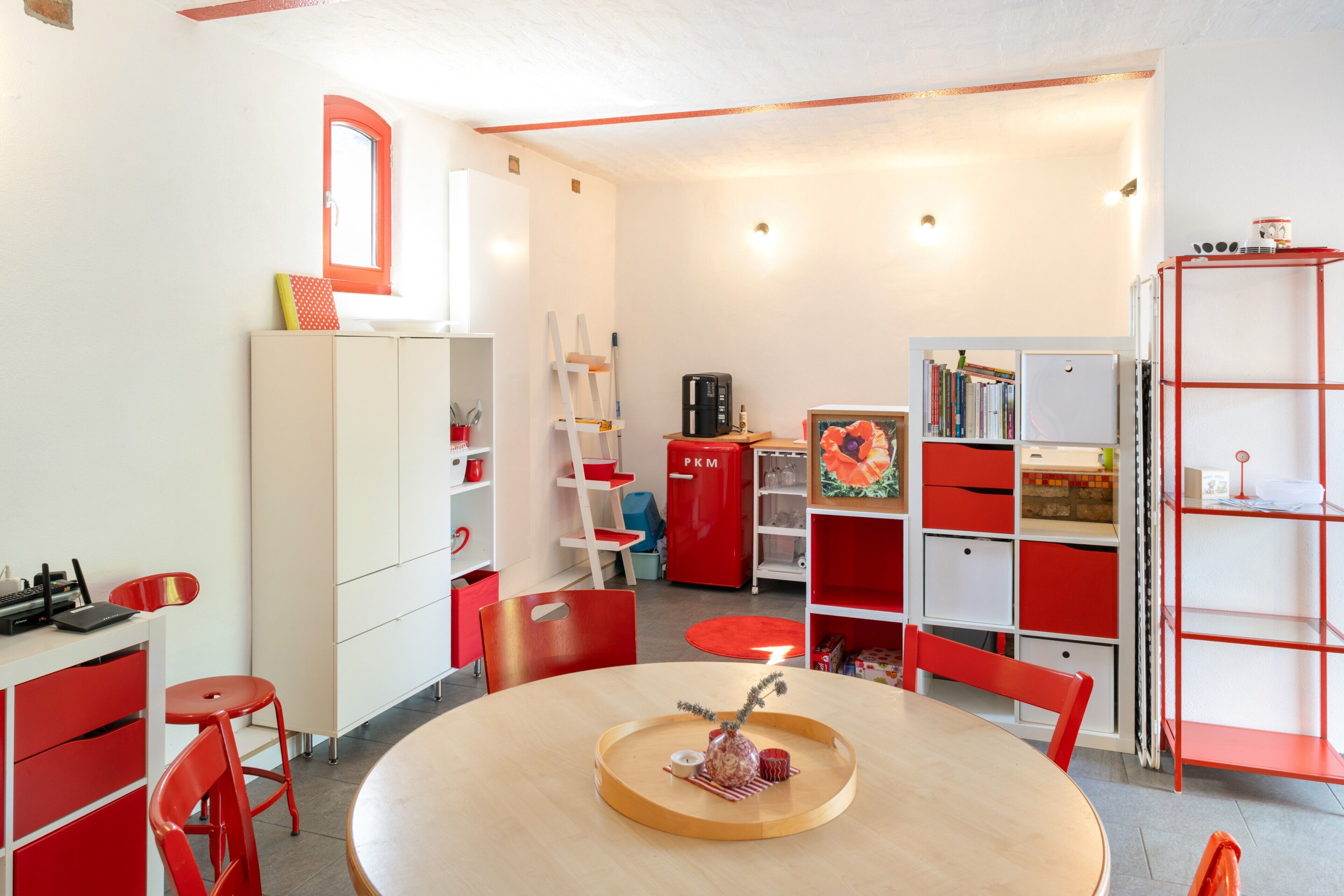Ein Zimmer mit einem runden Tisch, roten Stühlen, einem Bücherregal und einem Schrank.