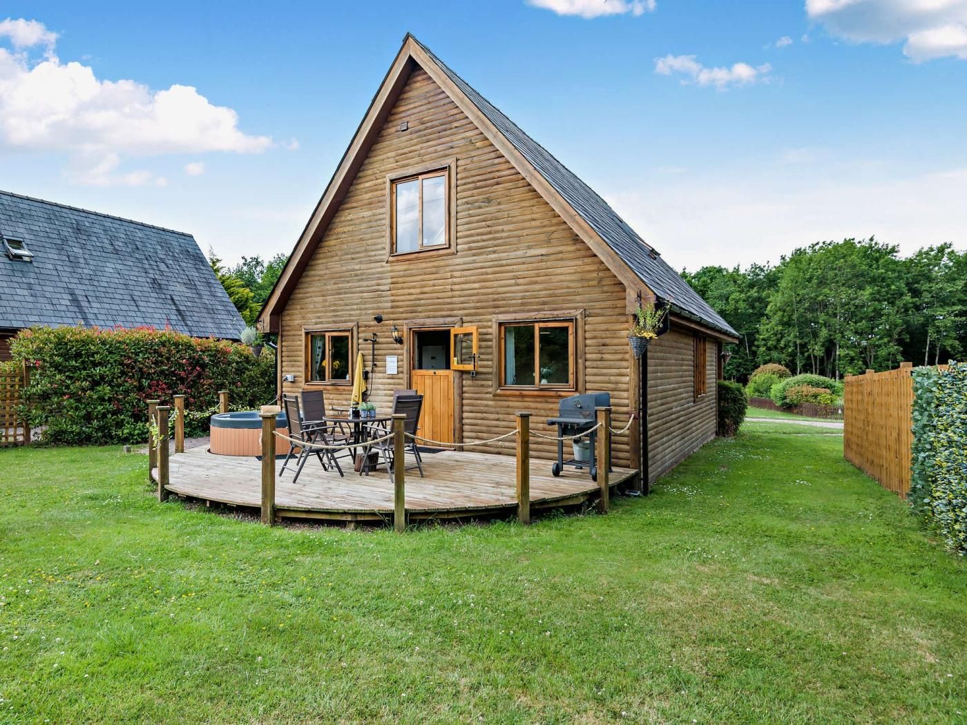 Una cabaña de madera con terraza, zona de barbacoa y un pequeño espacio de estar al aire libre.