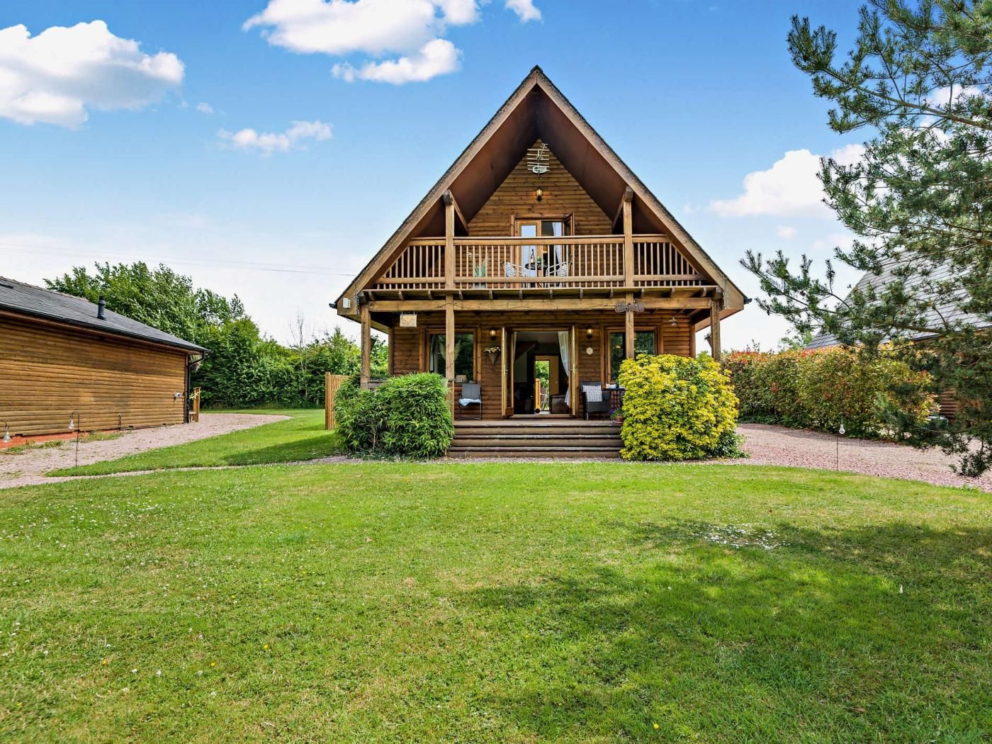 A wooden cabin with a balcony, a front porch, and a well-maintained lawn.
