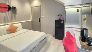A modern hotel room with a bed, a desk, a refrigerator, and a red chair. - ApecHotel284 (Ho Chi Minh City)