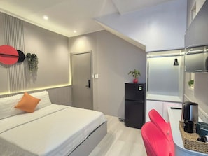 Una camera d'albergo moderna con un letto, una scrivania, un frigorifero e una sedia rossa.