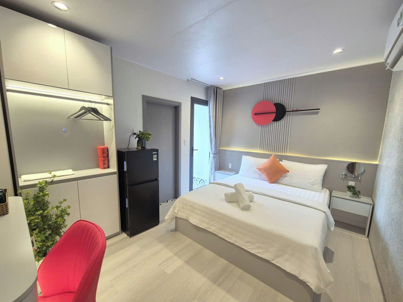Ein modernes Hotelzimmer mit einem Bett, einem Schreibtisch, einem Sessel, einem Kühlschrank und einer Wanduhr.