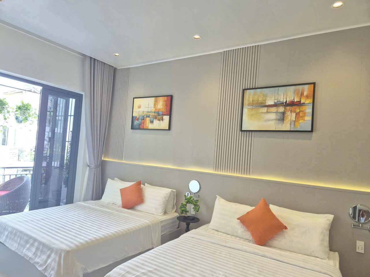 A hotel room with two beds, a large window, and two wall-mounted paintings.