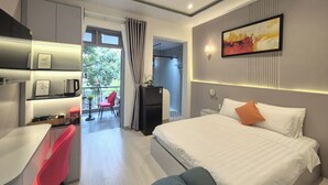 A modern hotel room with a bed, desk, and chair, a small kitchenette, and a view of the outdoors. - ApecHotel284 (Ho Chi Minh City)