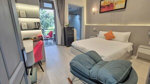 A modern bedroom with a bed, a seating area, a desk, and a shower. - ApecHotel284 (Ho Chi Minh City)