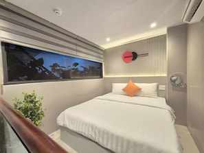 Una camera d'albergo moderna con un letto grande, un comodino, una sveglia a parete e una finestra con vista.