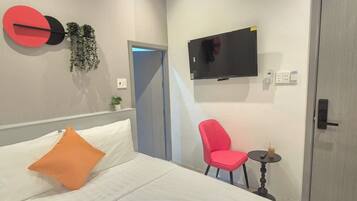 Ein Hotelzimmer mit einem Bett, einem roten Sessel, einem kleinen Tisch mit Fernbedienung, einem an der Wand befestigten Fernseher und einer Tür.