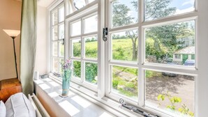 A room with a large window, a radiator, a lamp, and a vase with flowers. - 2 Bed in Beaworthy (oc-77555) (Black Torrington)