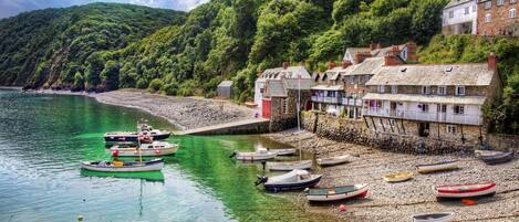 A coastal village with boats docked along the shore, stone buildings, and a rocky beach.