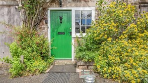 A green door with a window above it, surrounded by greenery and a stone wall. - 2 Bed in Beaworthy (oc-77555) (Black Torrington)