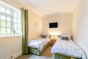A bedroom with two beds, a window with curtains, a wall-mounted TV, and a radiator.