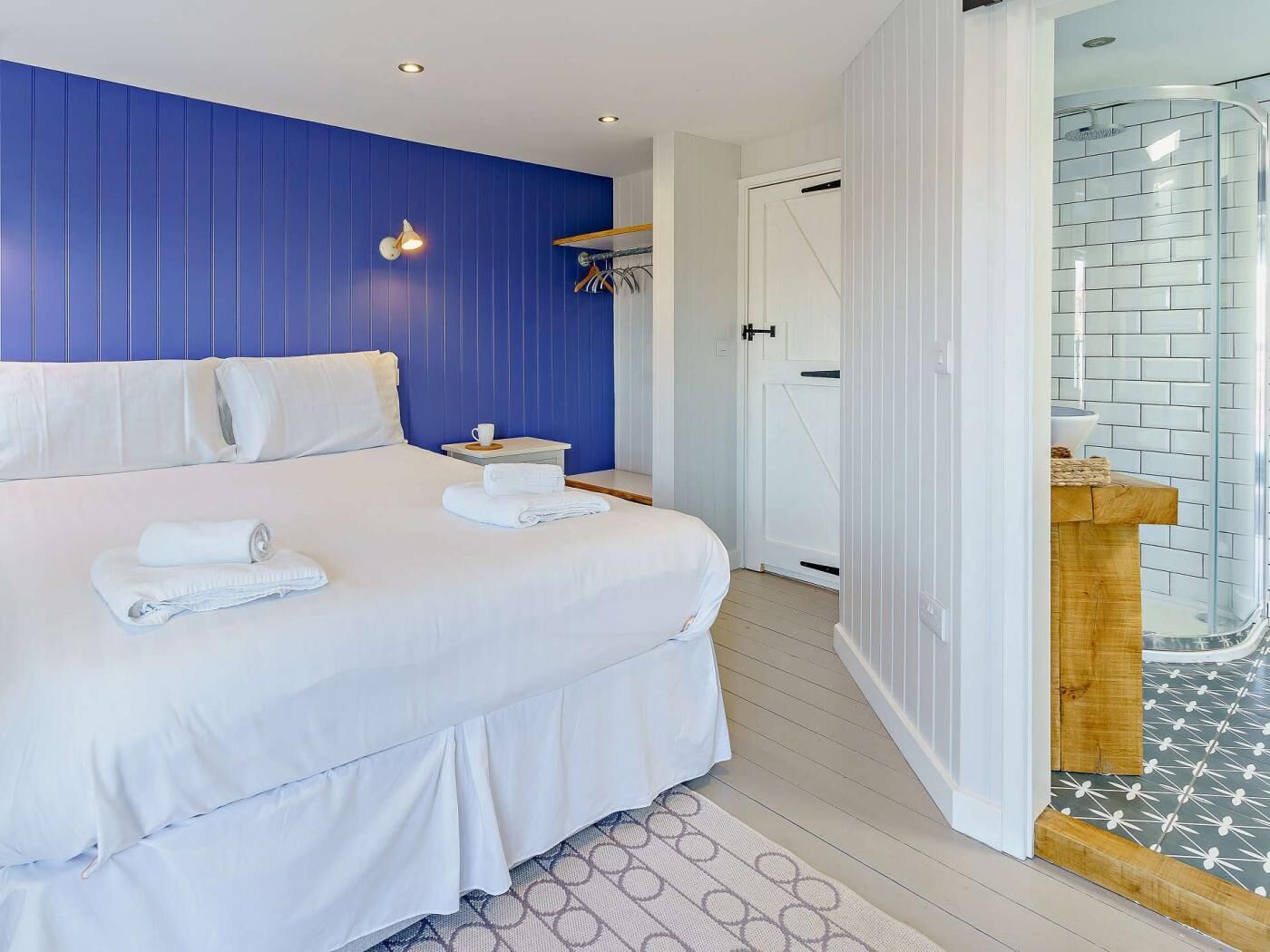 A hotel room with a bed, a bedside table, a white door, and a bathroom with a glass shower enclosure.