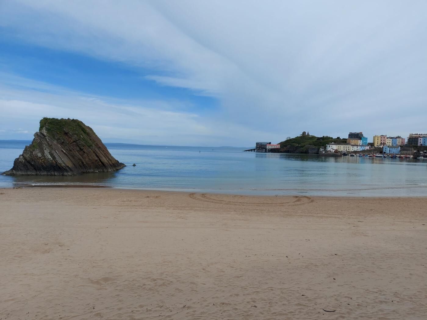 A sandy beach with a rocky outcrop and a small island with buildings.