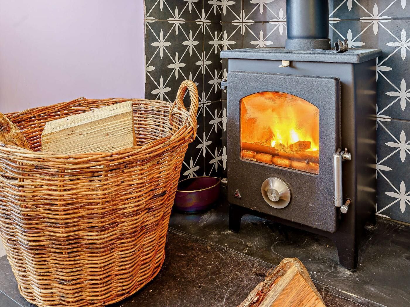 A wicker basket with firewood, a wood-burning stove, and a tiled wall with a geometric pattern.