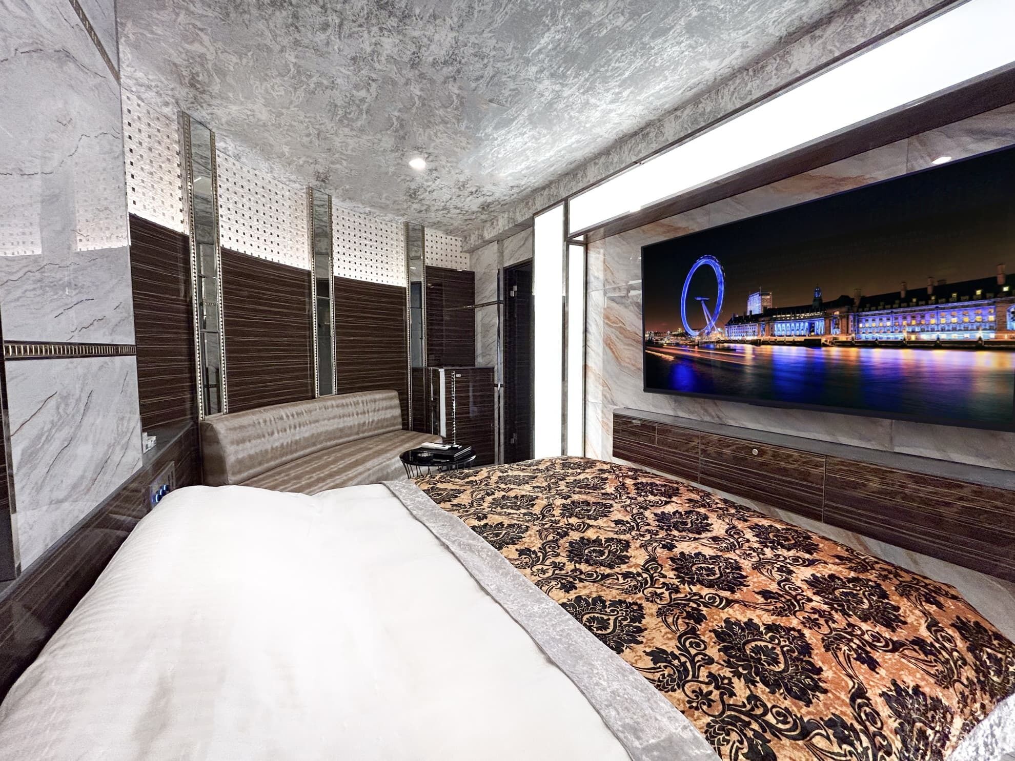 A modern hotel room with a large bed, a television displaying a cityscape, and a view of a Ferris wheel.