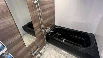 A bathroom with a glass shower enclosure, a black bathtub, and a tiled floor.