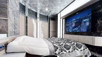 Een moderne slaapkamer met een groot bed, een televisie aan de muur en uitzicht op een stadslandschap.