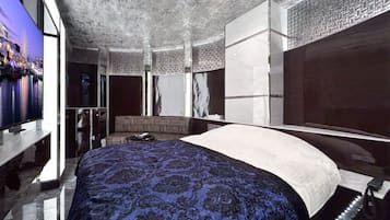 A modern bedroom with a large bed, a TV, and a patterned carpet.