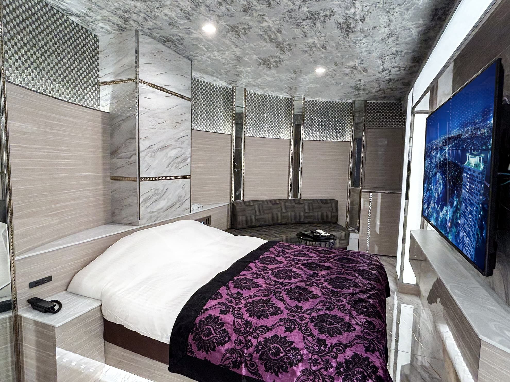 A modern hotel room with a large bed, a sofa, a TV, and a cityscape view.