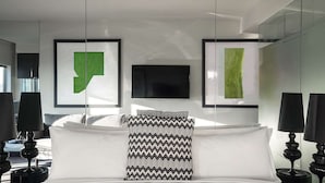 Una habitación de hotel moderna con una cama, dos cuadros abstractos enmarcados, un cojín decorativo blanco y negro y dos lámparas negras sobre mesitas de noche.