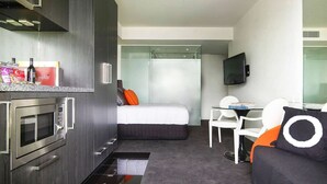 Habitación de hotel compacta con kitchenette, cama, televisor y un pequeño comedor.