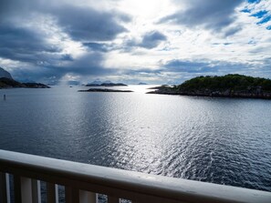 A calm sea with distant islands, a wooden railing, and a cloudy sky. - Seaview apartment in Henningsvær (Vågan)