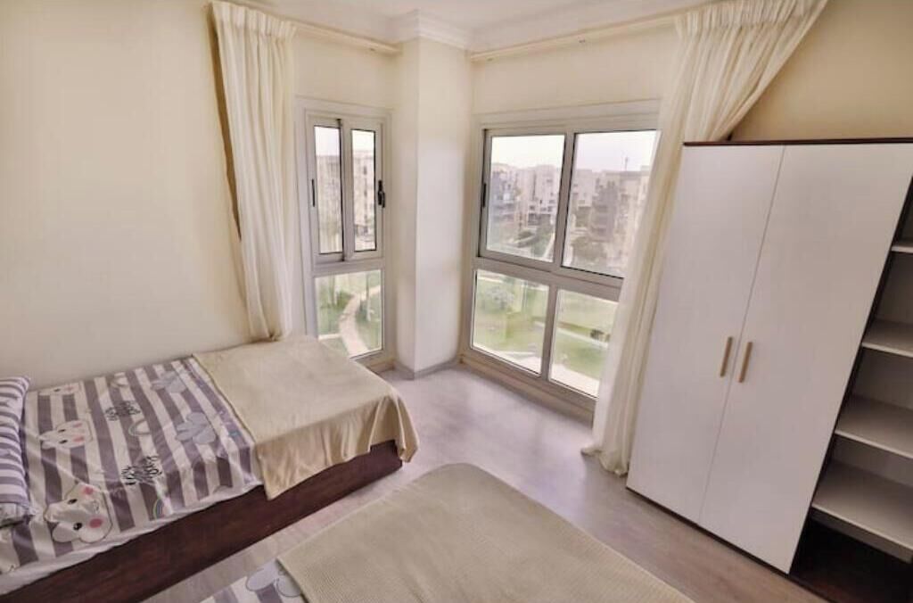 Ein Schlafzimmer mit einem Bett, einem Kleiderschrank und einem Fenster mit Blick auf Gebäude.