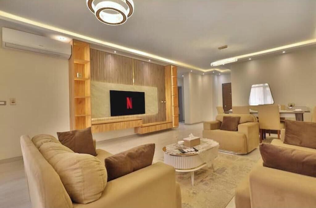A modern living room with a flat-screen TV, comfortable sofas, a coffee table, and a built-in bookshelf.
