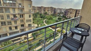 Een balkon met een tafel en stoelen, uitkijkend op een woongebied met meerdere appartementencomplexen en een groen park.