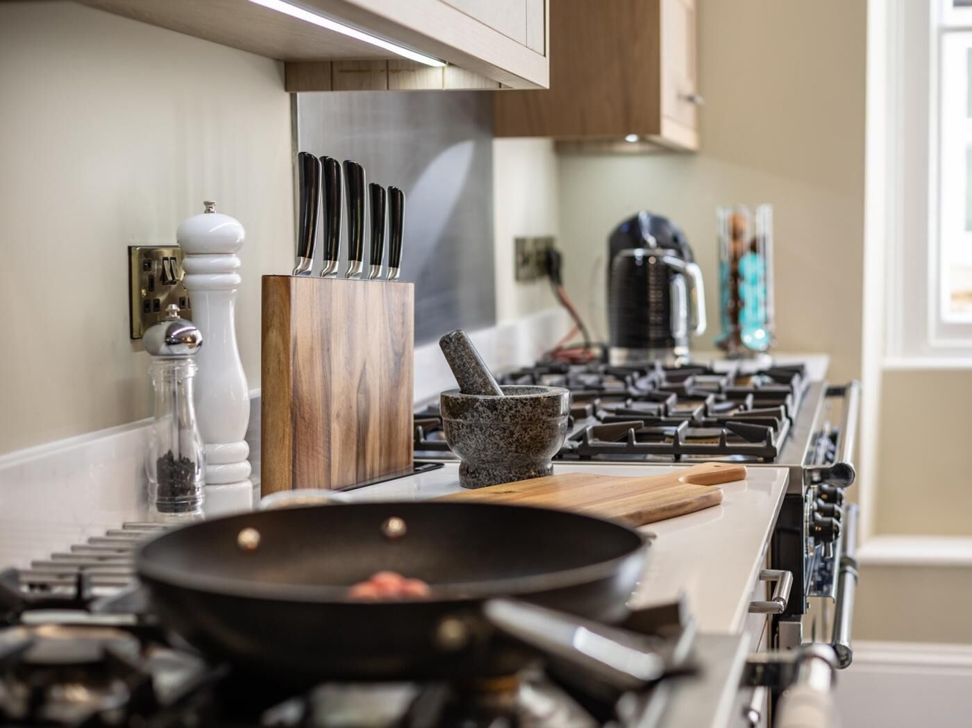 A kitchen with a stove, a frying pan, a mortar and pestle, a salt shaker, and a knife block.