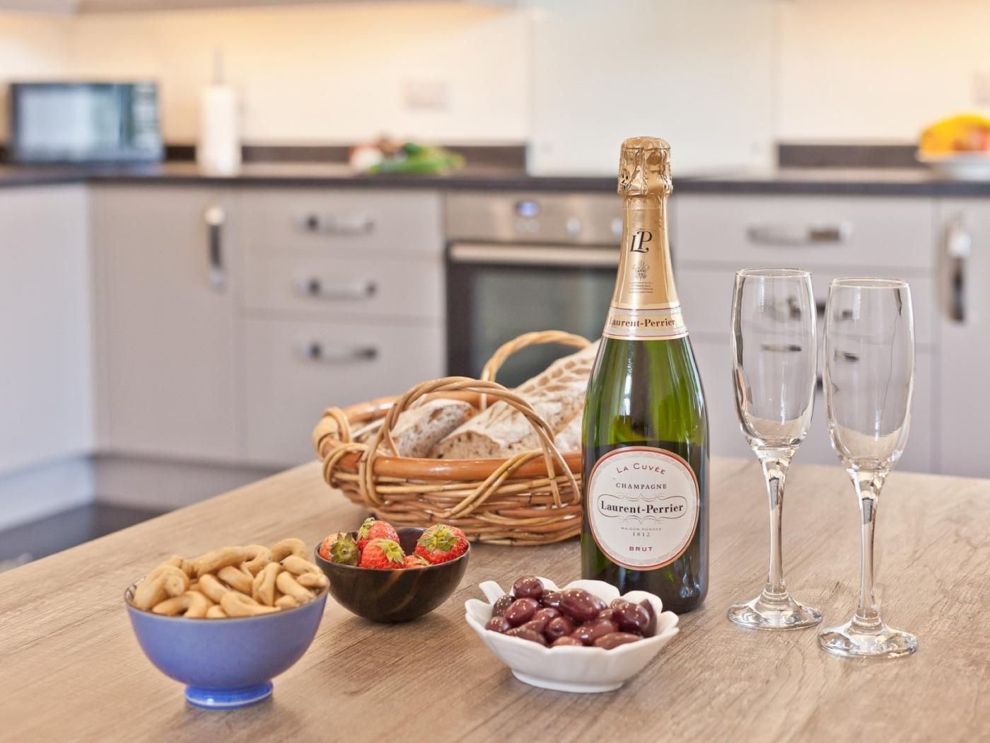 A kitchen counter with a bottle of champagne, two glasses, and bowls of snacks.