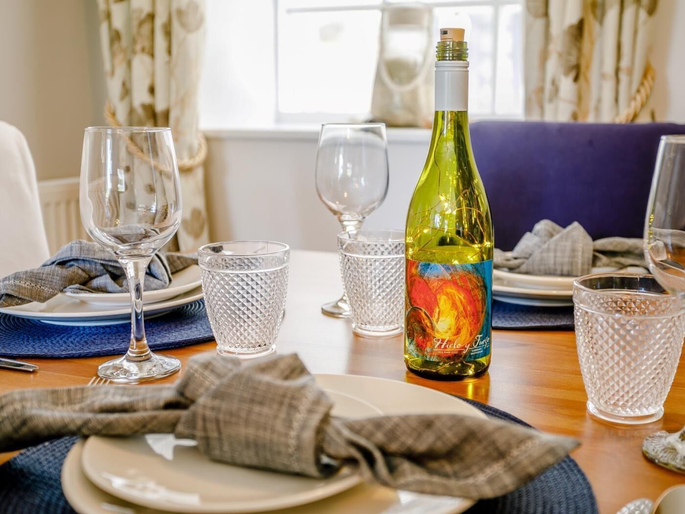 A dining table set with plates, glasses, and a bottle of wine.